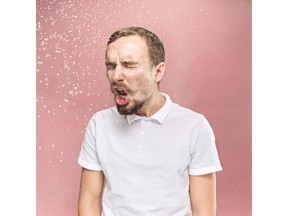 Young funny handsome man with beard and mustache sneezing with spray and small drops, studio portrait on pink background. Comic, caricature, humor. illness, infection, ache. Health concept