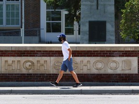A pedestrian wears a mask as they walk past the Western Canada High School sign in Calgary on Wednesday, July 22, 2020.