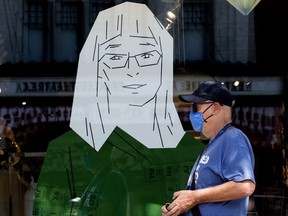 A pedestrian, wearing a mask to protect against COVID-19, walks past a poster of Alberta's Chief Medical Officer of Health Dr. Deena Hinshaw, in the window of Vivid Print, 10342 82 Ave., Wednesday July 29, 2020.