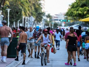 In this file photo a man rides a bicycle as people walk on Ocean Drive in Miami Beach, Florida on June 26, 2020. - Florida has registered more than 15,000 new cases of coronavirus in a day, easily breaking a record for a US state previously held by California, according to official numbers published on July 12, 2020