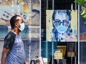 A person wearing a face mask passes by Sol Optix on 17 Ave. S.W. where a mask is put on a painting behind the window as the store requires all persons to wear face covering on Friday, July 31, 2020.