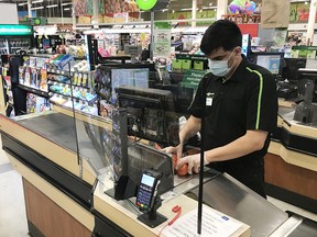 An employee is working behind a plastic shield at a grocery store in North Vancouver on March 22, 2020. These regular Canadians are the real heroes, says columnist Chris Nelson.