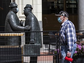 A masked pedestrian walks by the Conversation sculpture on Stephen Avenue in Calgary while one of the statues is wearing a mask on Monday, August 10, 2020.