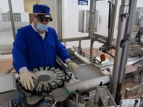 A worker wearing personal protective equipment (PPE) adjusts ampoules in a labeling machine during production of the 'Gam-COVID-Vac' COVID-19 vaccine, developed by the Gamaleya National Research Center for Epidemiology and Microbiology and the Russian Direct Investment Fund (RDIF), at JSC Binnopharm pharmaceutical complex, operated by Sistema PJSFC, in Zelenograd, Russia, on Friday, Aug. 7, 2020.
