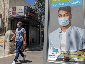 A mask-clad man walks past a billboard showing other mask-clad faces and adequate social distance measures, raising awareness about Covid-19 coronavirus pandemic precautions, in the Beit Hanina neighbourhood in Israeli-annexed East Jerusalem, on August 17, 2020.