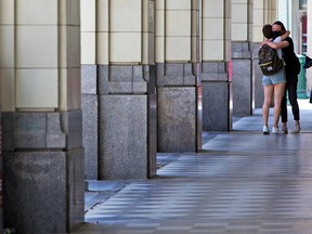 Friends greet each other with a hug under the arches of the Hudson’s Bay store in downtown Calgary on Thursday, August 6, 2020.