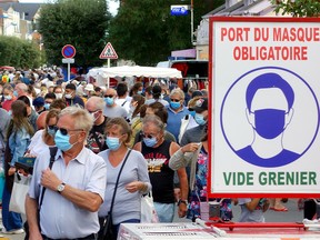 Pedestrians wearing protective face masks walk behind a COVID-19 information sign during the annual summer flea market as France reinforces mask-wearing as a part of efforts to curb a resurgence of the coronavirus disease (COVID-19) across the country, in Merville-Franceville-Plage, France, August 23, 2020.