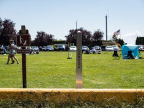 The COVID-19 pandemic has meant the Canada - U.S. border has been closed to regular cross-border shopping trips and vacations since May, and many American businesses near the border say they miss both the revenues and the Canadians. A Canada-U.S. border marker is seen in Surrey, B.C., as people gather at Peace Arch Historical State Park in Blaine, Wash., Sunday, July 5, 2020.