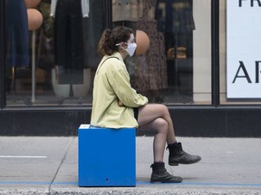 A woman wears a face mask as sits outside a clothing store in Montreal, Saturday, Aug. 22, 2020.