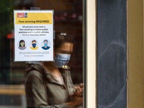 A woman wearing a face mask passes by Vine Arts Wine and Spirits on 17th Avenue S.W. where a sign requires customers to wear face coverings on Friday, July 31, 2020.