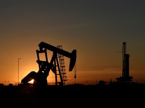 FILE PHOTO: A pump jack operates in front of a drilling rig at sunset in an oil field in Midland