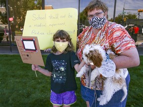 Minel, 10, and Maren Auckerman, along with their dog Aven, protest outside the offices of Calgary MLAs Jason Copping and Jason Nixon on Friday, Aug. 21, 2020.