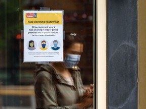 A person wearing a face mask passes by Vine Arts Wine and Spirits on 17 Ave. S.W. where a sign behind the window requires customers to wear a face covering on Friday, July 31, 2020. Tomorrow face coverings in public indoor spaces and vehicles becomes mandatory in Calgary. Azin Ghaffari/Postmedia