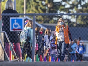 Students wait in line to be ushered into Westgate School by staff wearing face coverings while they are offered hand sanitizer on their first day back on Tuesday, Sept. 1, 2020.