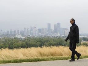 A pedestrian walks on the Valleyview Park pathway with a smoke-covered Calgary skyline in the background on Monday, Sept. 14, 2020.