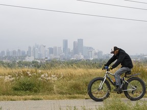 A cyclist moves along the Valleyview Park pathway with a vague, smoke-covered Calgary skyline in the background on Monday, September 14, 2020.