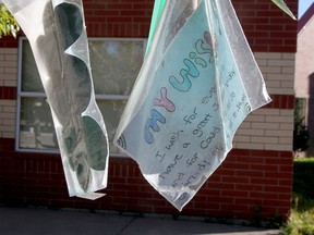 Student wishes hang in plastic bags from a tree in front of Fish Creek School in southeast Calgary on Aug. 22, 2020.