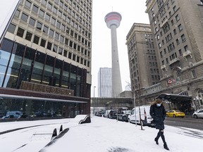 A masked pedestrian walks in downtown Calgary on a snowy morning on Wednesday, Oct. 21, 2020.