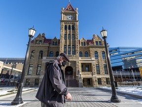A masked pedestrian walks in front of the old city hall in downtown Calgary on Monday, November 23, 2020.