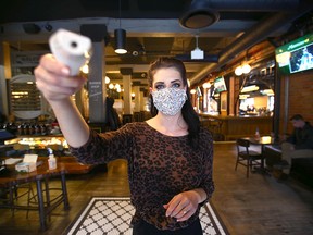Ashlynn Harris, Events Manager at Last Best Brewing on 11 Ave SW in Calgary, demonstrates how a customer's temperature is taken upon entry to the establishment on Friday, November 13, 2020. The temperature is taken on either the forehead or wrist. Masks and sanitizer is also available upon entry and they request contact information as well.