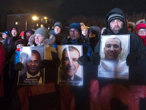 People hold pictures of the victims at a vigil to commemorate the one-year anniversary of the Quebec City mosque shooting, in Quebec City, Jan. 29, 2018.