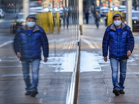 A masked pedestrian walks beside a reflective glass building in downtown Calgary, on Wednesday, December 2, 2020.