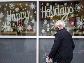 A masked pedestrian in front of a holiday sign on a shop window on 16 Ave. S.W. on Tuesday, Dec. 8, 2020.