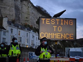 Police officers stand on duty at beneath a sign reading "Testing to Commence", at the entrance to the Port of Dover in Kent, south east England, on Dec. 23, 2020, where COVID-19 testing is set to begin on drivers who have been queueing to leave the UK. - France and Britain reopened cross-Channel travel on Wednesday after a 48-hour ban to curb the spread of a new coronavirus variant but London has warned it could take days for thousands of trucks blocked around the port of Dover to get moving.