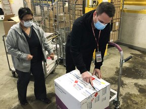 Sheila Mondragon and Robbie Shields (right), with AHS Supply Management, accept the first delivery of the Moderna COVID-19 vaccine in Calgary on Tuesday, Dec. 29, 2020. The first shipments of the Moderna vaccine have arrived in Alberta and will be rolled out to long-term care and designated supportive living sites across the province.