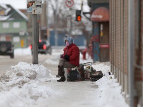 A person wears a mask while sitting on a shopping cart full of personal items, in Winnipeg. Saturday, Dec. 26, 2020.