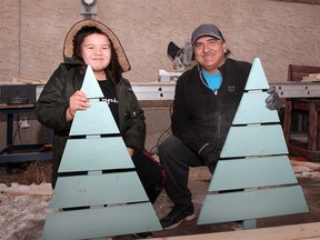 Derek McGills and his grandson Tayson Big Plume pose for a photo with hand built wooden Christmas trees in their SW backyard. The trees are left blank for families to paint together as a fun holiday event. Tuesday, Dec. 15, 2020.
