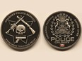 A Calgary Police Service firearms training team challenge coin depicts a bullet hole through a skull, surrounded by three guns and the phrase "saving lives." Calgary police have prohibited further distribution of the coin, calling the design "obviously offensive."