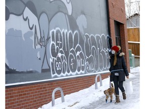Sandra Chung walks by graffiti, which was sprayed over existing artwork, on the side of the Village Ice Cream store in Bridgeland on Monday, Dec. 28, 2020.