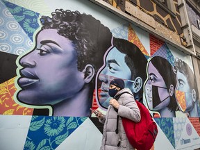 A pedestrian wearing a mask walks past a mural by artist Gosia Koma Rski in Toronto  on Thursday, Dec. 3, 2020.