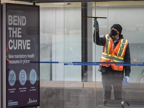 A worker cleans a glass bus stop with a COVID informative poster attached to it in downtown Calgary on Tuesday, Jan. 12, 2021.