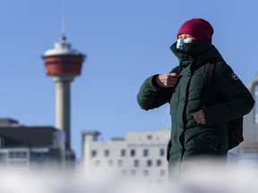 A masked pedestrian walks on the Bow River pathway with the Calgary Tower in the background on Wednesday, Jan. 20, 2021.