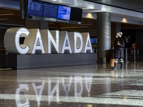 A masked woman views the arrivals board at Calgary International Airport on Friday, Jan. 8, 2021.