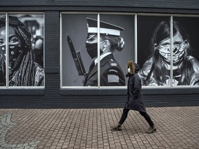 A pedestrian wearing a mask walks by a photography exhibit  at Toronto's Harbourfront Centre on Monday, Jan. 4, 2020.