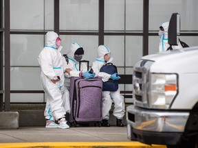 People wearing protective face masks, goggles and Tyvek suits who said they traveled from Colombia wait for a car rental company shuttle, after arriving at Vancouver International Airport in Richmond, B.C., on Thursday, December 31, 2020.