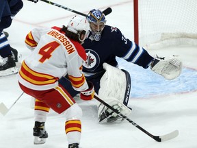 Winnipeg Jets goaltender Connor Hellebuyck is at the mercy of Calgary Flames defenceman Rasmus Andersson during NHL action in Winnipeg on Thursday, Jan. 14, 2021.