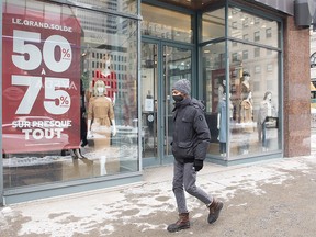 A man wears a face mask as he walks by a storefront window in Montreal, Sunday, Feb. 7, 2021, as the COVID-19 pandemic continues in Canada and around the world. Non-essential businesses such as stores, museums and hair dressers will be allowed to reopen as of Feb. 8 in Quebec. The province has been under lockdown since Dec. 25, 2020.