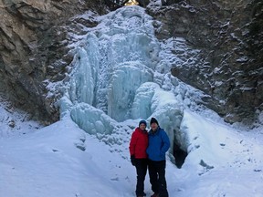 An image of a couple standing in front of Star Creek Falls in winter in Crowsnest Pass, Alberta.