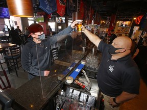 Mark Milne gets a beer from owner Mike Shupenia at Side Street Pub and Grill in Kensington during the next stage of reopening in Calgary on Monday, February 8, 2021.
