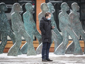 A pedestrian wearing a mask checks his phone while waiting to cross a street in Calgary on Thursday, Nov. 19, 2020.