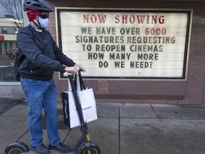 A man on a scooter passes by a sign posted by a theatre protesting COVID-19 restrictions in Vancouver on Jan. 15, 2021.