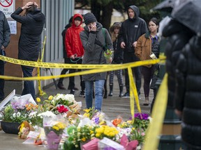 People lay flowers at a makeshift memorial outside of the Lynn Valley Library in North Vancouver, B.C., Sunday, March 28, 2021. The memorial is for stabbing victims that were attacked by a man with a knife on Saturday, sending several to hospital and leaving one dead.