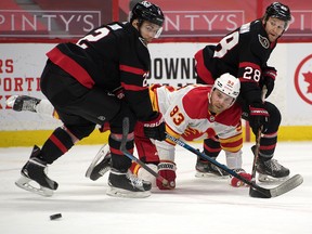 Flames centre Sam Bennett is knocked off the puck by two Ottawa Senators in the first period at Canadian Tire Centre on Feb. 25, 2021.