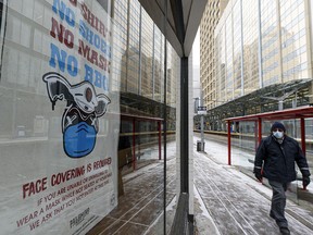 A masked pedestrian walks in front of a sign requiring visitors to wear a mask at a restaurant in downtown Calgary on Tuesday, Jan. 26, 2021.