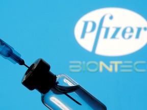 A vial and syringe are seen in front of a displayed Pfizer and Biontech logo