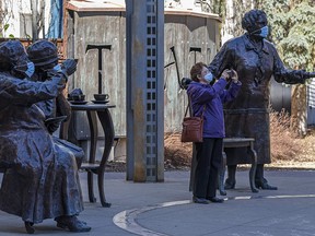 A woman takes photos of the Famous Five Statue which has been dressed up with masks on Friday, April 16, 2021.